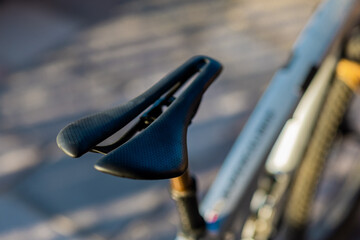 A close-up, shallow-depth-of-field shot of a sleek, black aerodynamic bicycle saddle mounted on a high-performance mountain bike, featuring a central cutout and textured grip for racing comfort.