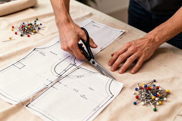 Hands cutting fabric along sewing pattern lines.