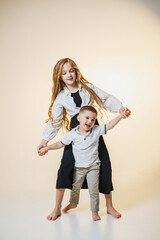 Joyful siblings share a playful moment in a serene studio setting with soft lighting and a warm, inviting background