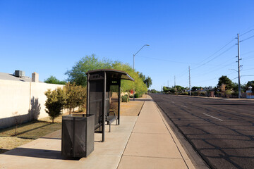 Bright sunny Sunday morning at empty roadside city bus stop with cozy waiting bench and modern shade shelter, Phoenix, Arizona; copy space