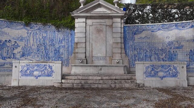 Upward pan of historic azulejo-tile fountain at Pa&ccedil;o de Arcos with blue-and-white murals and Portuguese pavement in front.