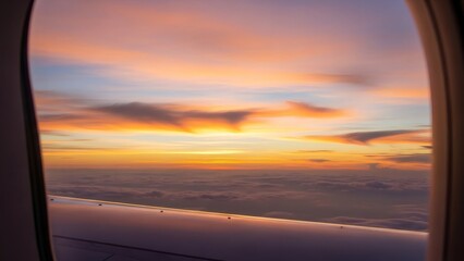 View of vibrant sunset sky and soft clouds from an airplane window, showcasing golden light over the wing for travel and adventure