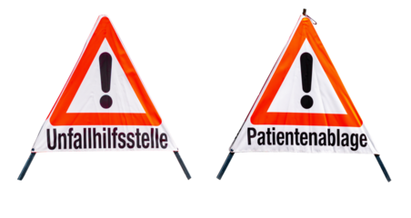 Two triangular warning signs with large exclamation marks and the texts "unfallhilfsstelle" and "patientenablage", foldable stands with reflective fabric, clear view of typography and graphics.