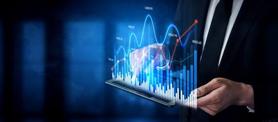 A businessman in a suit is holding a tablet with a digital display of financial growth charts and data visualizations, emphasizing modern technology in business analytics. Scalp