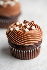 Chocolate cupcake topped with smooth swirled chocolate cream cheese frosting and white chocolate curls on a light stone background.