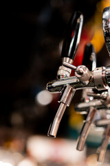 A close-up, selective focus shot of shiny, metallic beer taps with black handles installed at a bar...