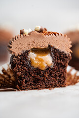 Cut chocolate cupcake revealing gooey caramel nut filling topped with chocolate cream cheese frosting, styled as a rich indulgent dessert close up.