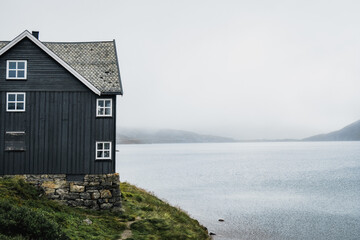 Typical norwegian grey cabin next to a lake with fog