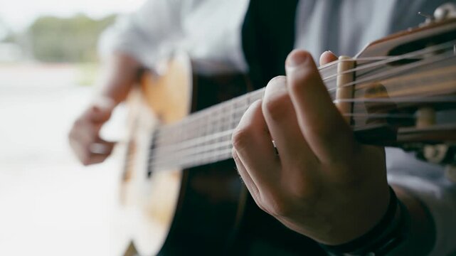 Close up of a musician's hands playing an acoustic guitar. The guitarist is fretting chords and strumming the strings, creating music