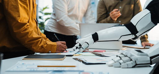 A scene depicting a modern office meeting where a robotic arm assists a human team. This image illustrates advanced technology in collaboration and innovative approaches to teamwork.Noogenesis