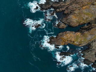 Waves crash against rugged cliffs of a remote coastline at sunset, revealing the beauty of nature's raw forces and tranquil waters