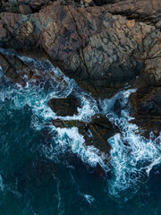 Waves crash against jagged rocks along a rugged coastline at sunset, creating a dramatic scene of nature s raw power and beauty
