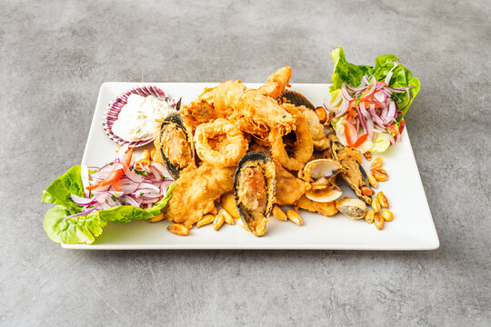 A generous portion of mixed fish jalea, with chunks of white fish, shellfish, and crispy fried calamari, served on a bed of red onion and accompanied by salsa criolla