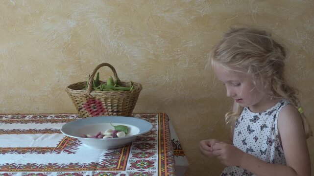 little girl peels beans from pods, Child helps in kitchen, cleaning green beans