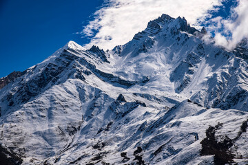 Naklejka premium Tilicho Peak and surrounding alpine ridges near Muktinath, Nepal. Dramatic Himalayan mountain scene with sharp rock formations, snow-covered slopes, and deep blue sky, 