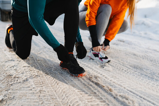 Close-up of two runners tying shoelaces on sneakers before a winter run in the snow.
