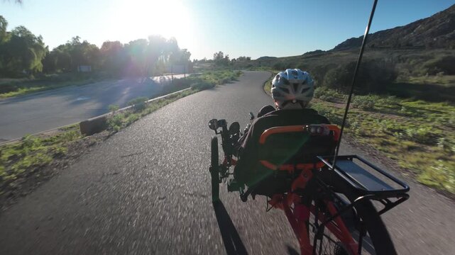 Senior man enjoys biking on a recumbent electric tricycle along a winding path under clear skies and bright sunshine in a park.