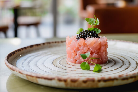 Exquisite toro tartare topped with black caviar. Minimalist Japanese-style gourmet appetizer with microgreens on a textured ceramic plate in a fine dining restaurant