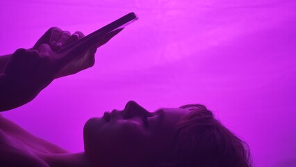 Silhouette of woman using a smartphone against a vibrant pink backdrop, highlighting digital...