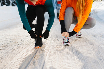 Close-up of two runners tying shoelaces on sneakers before a winter run in the snow.