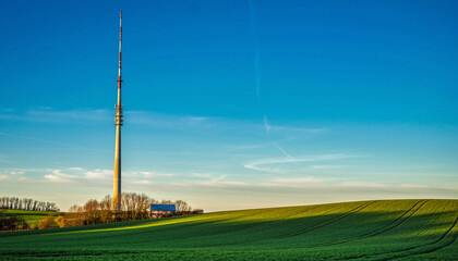 A tall communication tower stands in a vibrant green field under a clear blue sky.