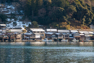 Row of traditional Funaya boathouses in the fishing village of Ine, their roofs lightly dusted with snow on a clear winter day. Ine, Kyoto, Japan.