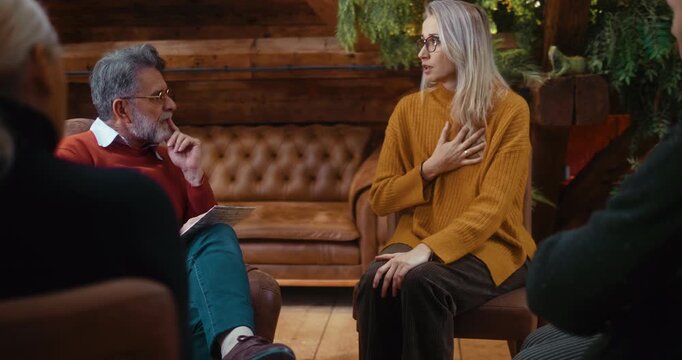 Honest female participant sitting and speaking about personal difficulties during group psychotherapy, sharing openly while receiving calm professional support in a safe environment.