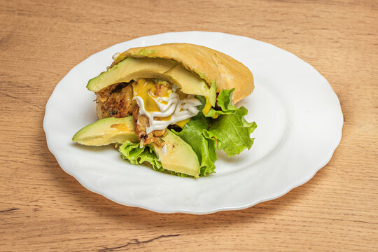 Pre-cooked cornmeal arepa filled with stewed chicken, cabbage salad, and homemade mayonnaise, cut in half.