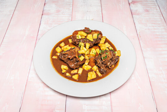 A hearty oxtail stew, accompanied by boiled potatoes and whole carrots that have absorbed the flavor of the rich, dark broth