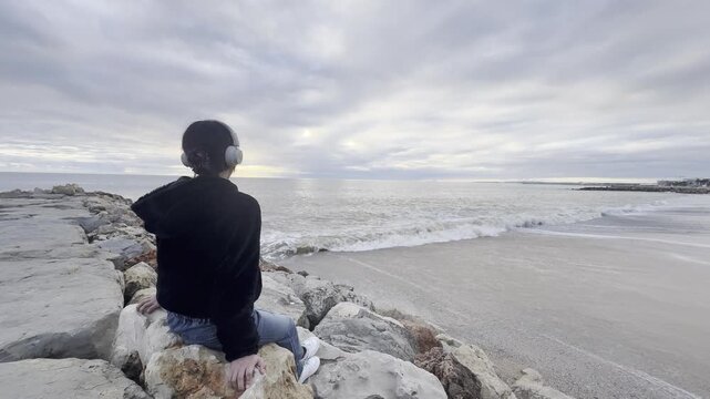 Teenager girl in yellow jacket sitting on a rock and looking at stunning nature background with ocean and cliffs. Travel and tourism. portugal. Dramatic sunset sky. Famous area.