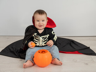 Cute caucasian boy in dracula halloween costume holding candy basket on white background. 