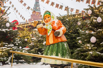 Moscow, Russia, 29 December 2025   Russian winter festival girl statue among decorated fir trees with string lights at a snowy Christmas market; Kremlin tower in the background, Moscow, Russia.