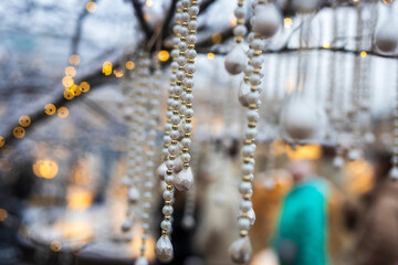 Close-up of pearl bead garlands and white hanging ornaments with warm bokeh lights in the background.