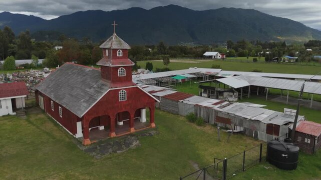 Aerial Close View of Historic Red Wood Church Against Mountain Range and Stormy Sky