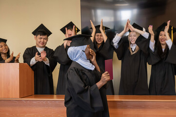 Happy African woman in hijab receiving diploma and classmates applauding her. 