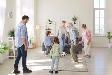 Fototapeta premium Large and positive family with kids actively playing football with ball together in the living room, enjoying leisure time and bonding through a lively game. Family unity and fun at home.