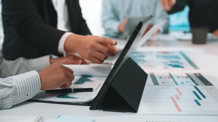 A diverse group of professionals collaborates at a modern office table, utilizing a tablet to analyze data charts, highlighting teamwork in strategic market planning. SACTR - Powered by Adobe