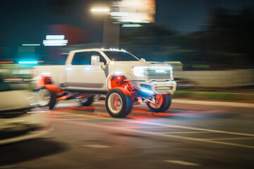 Fototapeta premium LOS ANGELES, CA - October 09, 2025: Custom GMC Sierra lifted lifestyle pickup truck with TIS Wheels driving on dark city street at night. Urban road background is blurred in motion.