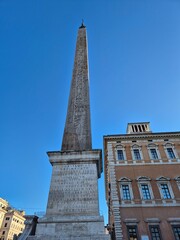 Rome, Italy - 14 January 2025. An Egyptian obelisk with Latin and hieroglyphic inscriptions rises next to the Basilica of San Giovanni in Laterano against a bright sky.