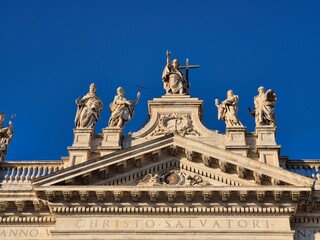 Rome, Italy - 14 January 2025. The upper pediment of San Giovanni in Laterano shows Christ with apostles holding religious symbols, carved in stone against a clear sky.