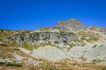 Rocky alpine slopes and mountain ridge in Five Polish Ponds Valley under clear blue sky