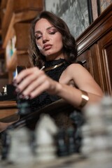 A beautiful brunette in a black evening dress plays chess. 