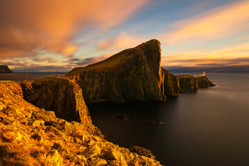 Golden sunset light on dramatic sea cliffs at Neist Point, Isle of Skye, with smooth ocean and glowing rocks, atmospheric coastal landscape for travel and nature background.