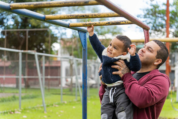 Father helping toddler playing on monkey bars