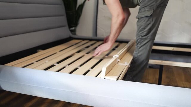 Self-assembly using a guide. House design. Close-up of a man's hands assembling a wooden bed using a screwdriver to insert screws into the bed frame.Collection of wooden furniture. Husband for an hour