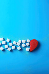 Red heart and sugar cubes symbolizing diabetes awareness on blue background with copy space for World Diabetes Day November 14