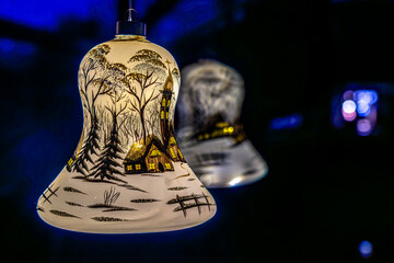 An artfully painted glass bell depicting a winter village and forest scene glows warmly against a dark, shimmering blue background