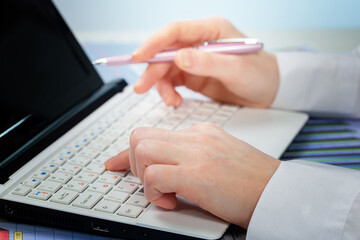 Fototapeta premium A woman working on an accounting report with a computer. Close-up of her hands.