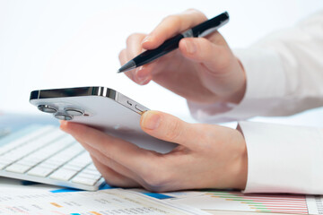 A woman works with a smartphone in the office, on a report. Close-up of her hands. 	