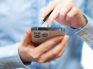 A woman works with a smartphone in the office, on a report. Close-up of her hands. 	